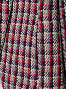 Close-up detail of multicolored tweed fabric blazer with green piping texture.
