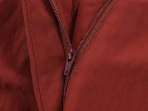 Close-up view of red casual pants zipper detail, highlighting fine stitching and texture.