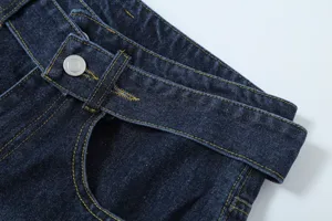 Close-up detail of dark blue denim trousers waist with contrast yellow stitching and metal button