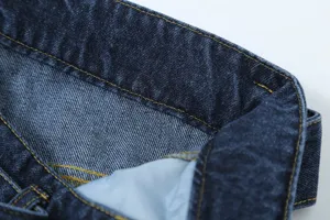 Close-up detail shot of dark blue denim trousers waistband, premium stitching texture.