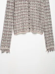 Close-up detail of women's tweed knitted cardigan featuring chic fringe cuffs and black buttons.
