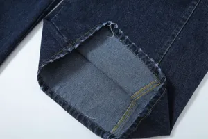 Dark blue denim trousers cuff detail, featuring distressed raw hem and precision stitching.