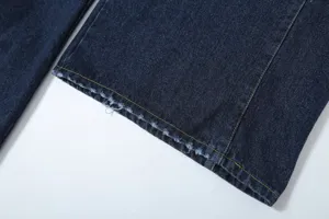 Close-up detail of dark blue denim trousers cuff with contrast yellow stitching and raw hem.