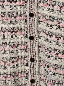 Detailed close-up view of womens chic tweed knit cardigan fabric texture with elegant black buttons.