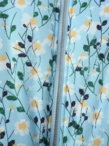 Close-up detail of light blue jacket with white daisy embroidery and metal zipper.