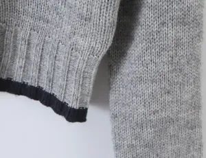 Close-up detail of grey knit sweater sleeve and ribbed cuff with contrast dark trim.