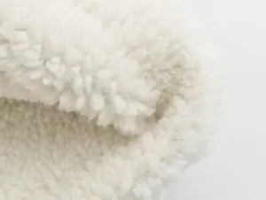 Detailed close-up view of white sherpa fleece fabric, soft fluffy teddy material for winter wear.