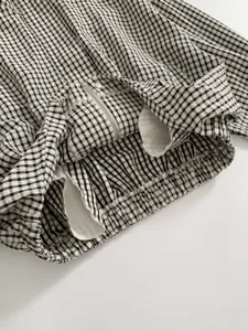 Close-up detail of the black and white gingham jacket hem, zipper, and pleated elastic design.