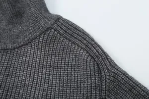 Close-up detail of dark grey ribbed knit sweater shoulder and high turtleneck collar.