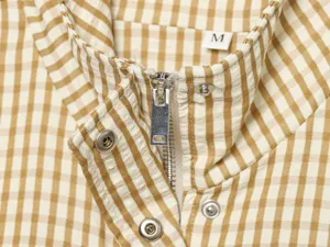 Close-up detail of yellow and white gingham jacket collar, metal zipper and button.
