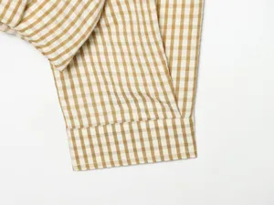Close-up detail of casual brown white gingham plaid jacket sleeve cuff texture fabric.