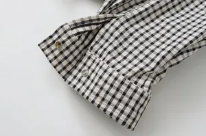 Black and white gingham jacket sleeve detail showcasing metallic snap buttons and fabric texture.