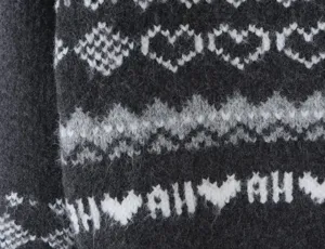 Close-up detail of a cozy knit sweater featuring classic Fair Isle patterns, hearts, and text.