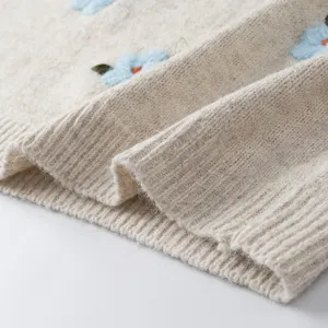 Primer plano detalle de chaleco de punto para mujer con bordado floral 3D beis.