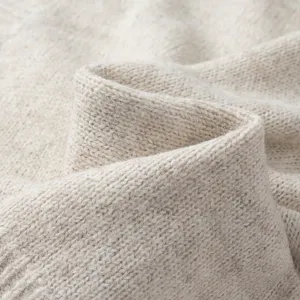 Vista detallada de tela de suéter de punto beige suave, mostrando textura y hilo finos.