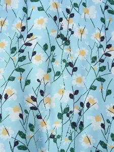 Close up view of light blue fabric featuring white daisy flower print and green leaves texture.
