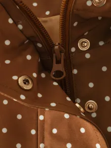 Close-up detail of women's brown polka dot jacket featuring zipper and metallic snap buttons.