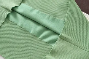 Close-up detail of green women knitted sweater showing fine ribbed texture and folded layer.