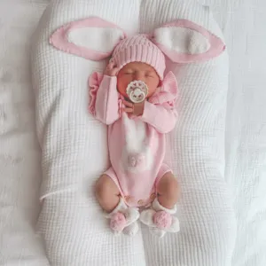 Detailed view of newborn pink knitted bunny romper and long-eared hat set in white baby nest