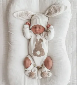 Close-up detail of newborn baby wearing cute bunny ear beanie and knit romper set in white lounger.