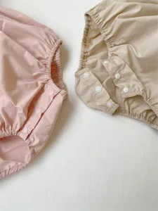 Detailed view of infant baby rompers with snap buttons in pink and beige colors soft fabric.