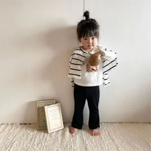 Detailed lifestyle shot of a baby wearing striped cardigan and black pants in a cozy room.