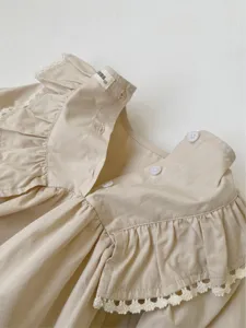 Detail view of baby girl ruffle romper in beige cotton with lace trim and back buttons.