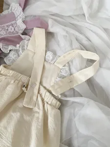 Close-up of beige baby suspender romper with delicate lace trim and button detail.