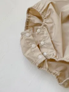 Infant baby romper detail shot, light beige cotton fabric with white snap buttons and ruffles.