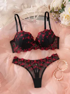 Details of black and red floral embroidered French bra and thong lingerie set on pink fabric.