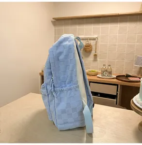 Side detail view of the stylish light blue checkered backpack on wooden table surface.