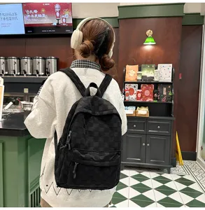 Detailed view of a casual black checkered backpack worn by a model in a stylish cafe setting.