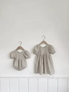 Detailed view of baby girl cotton embroidered bubble romper and dress in soft neutral beige.