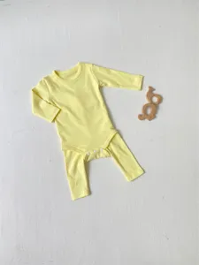 Detailed view of yellow long-sleeve baby bodysuit with snap closure and wooden teether prop.