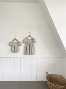 Detailed view of baby girl cotton floral embroidered dress and romper hanging on wooden hangers.