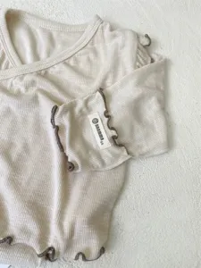 Infant baby ribbed cotton long sleeve top detail showing cute brown lettuce edge trim design.