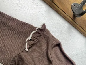 Brown ribbed baby long sleeve top detail close up with white ruffle shoulder trim cute.