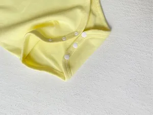 Soft yellow baby bodysuit detail shot featuring neat stitching and secure snap buttons.