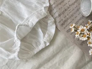 Detailopname van een witte babyromper met jacquardstof, drukknopen en fijne textuur.