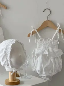 Detail van witte zomerromper voor baby met fijne textuur, mooie volant en bijpassend mutsje.