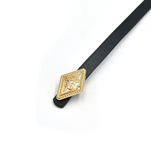 Close-up detail shot of black thin leather belt showing ornate gold rhombus metal buckle design.