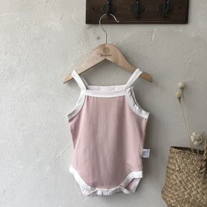 Details of the cute pink baby romper with white trim hanging on a wooden hanger with dry flowers.