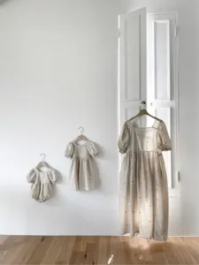 Detailed view of minimalist cotton embroidered toddler dresses and baby romper hanging on wall.