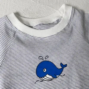 Close-up view of a baby summer striped top featuring a cute blue whale print and soft collar.