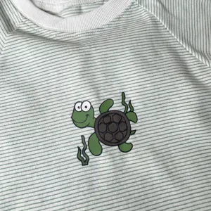 Baby striped t-shirt detail showing cute turtle graphic print and green white stripes fabric.