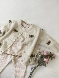 Close-up details of baby knitted cardigan and pants set with cute floral embroidery and ruffles.