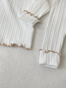 Close-up white baby long sleeve top brown lettuce edge ribbed fabric detail texture