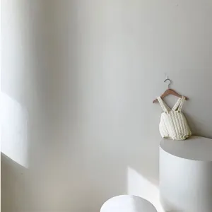 Close-up detail shot of cute quilted baby romper hanging on neutral minimalist studio wall.