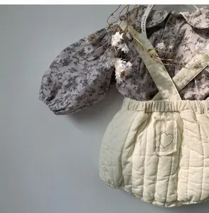 Infant padded baby romper detail shot featuring floral blouse and quilted strap shorts.