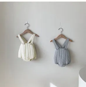 Detail view of thick quilted baby rompers hanging on wooden hangers in neutral tones.
